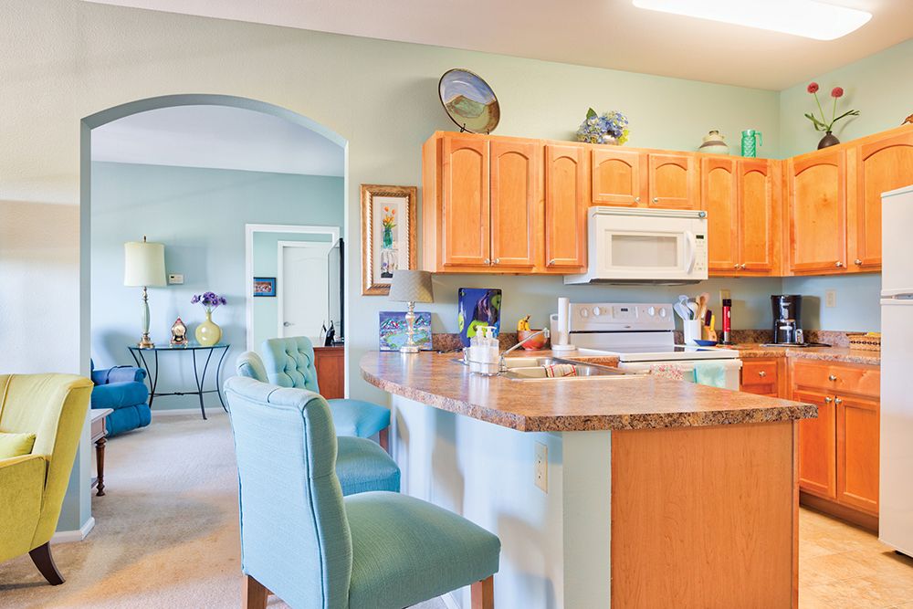 Bright kitchen interior with wooden cabinets and teal bar stools.