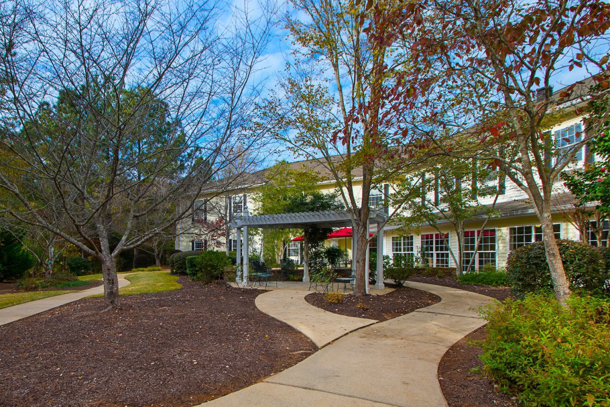 A well-maintained pathway leads to the entrance of a building surrounded by trees and landscaping on a clear day.