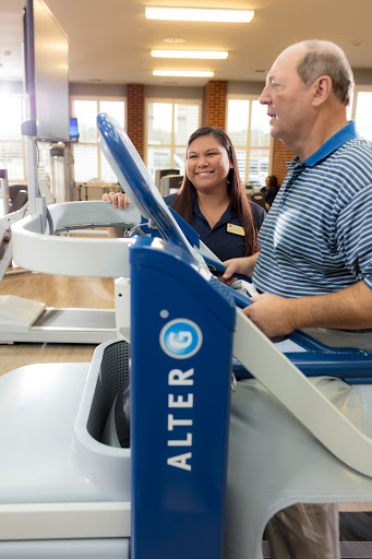 A fitness trainer assists a client on specialized exercise equipment in a rehabilitation setting.