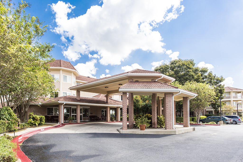 The image shows the entrance of a hotel building with a covered driveway and a clear blue sky overhead.