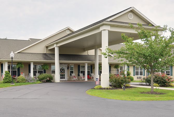 A view of a building entrance with a covered porch and landscaped surroundings.