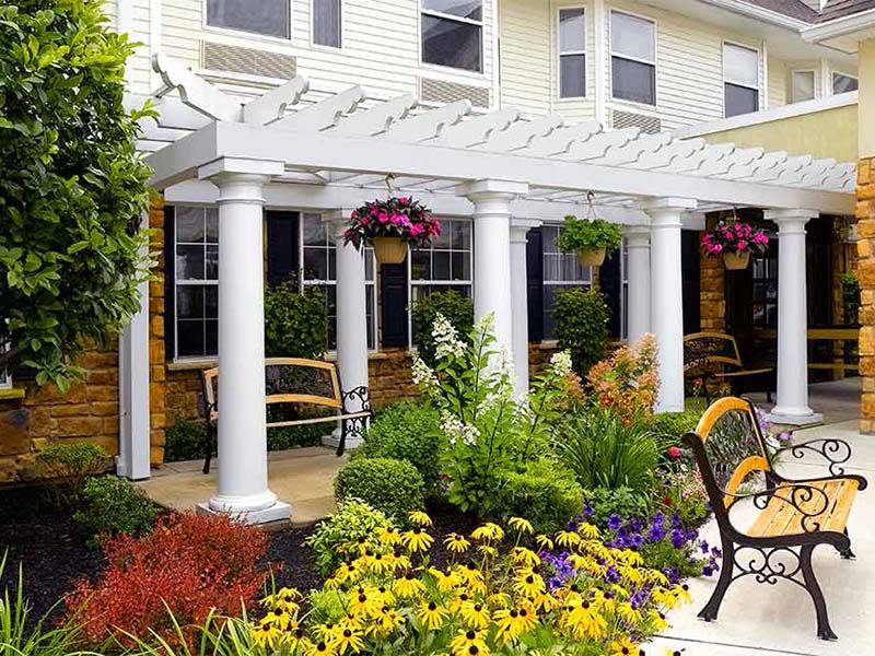 A beautiful garden with a pergola and vibrant flowers in front of a building.