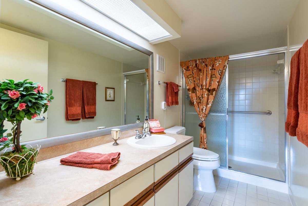 A well-lit bathroom with a large mirror, sink, and shower area.
