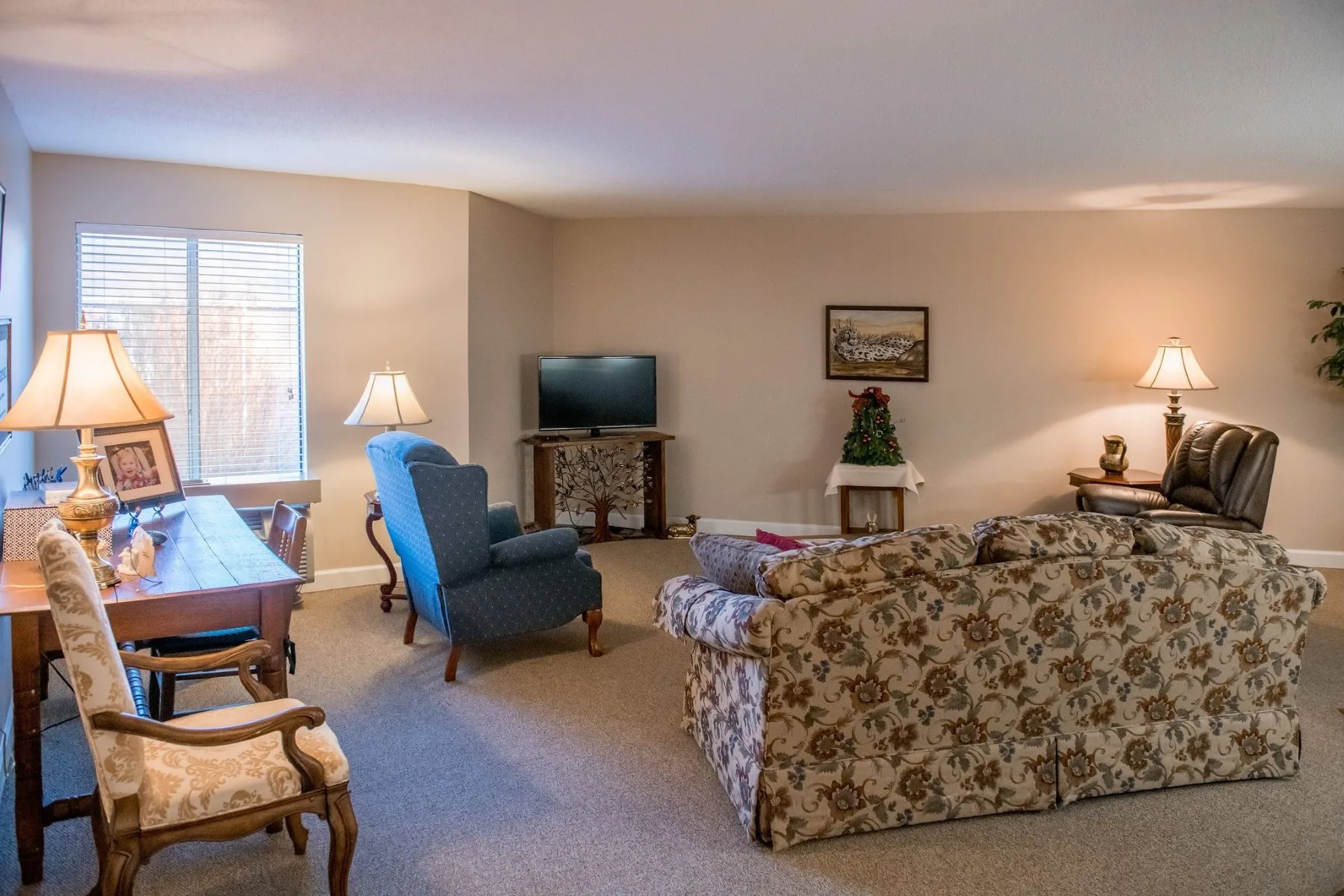 A cozy living room with a floral sofa, armchair, television, and warm lighting.