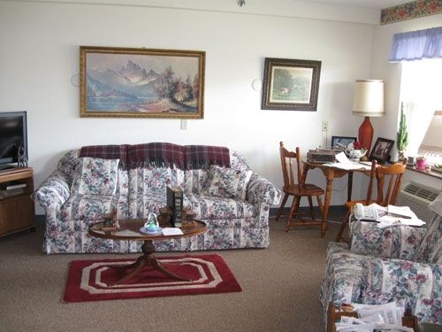 A cozy living room with a sofa, framed paintings, a lamp, and a small table.