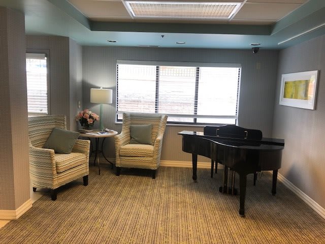 A cozy living room with a piano, two armchairs, a small table, and a lamp by the window.