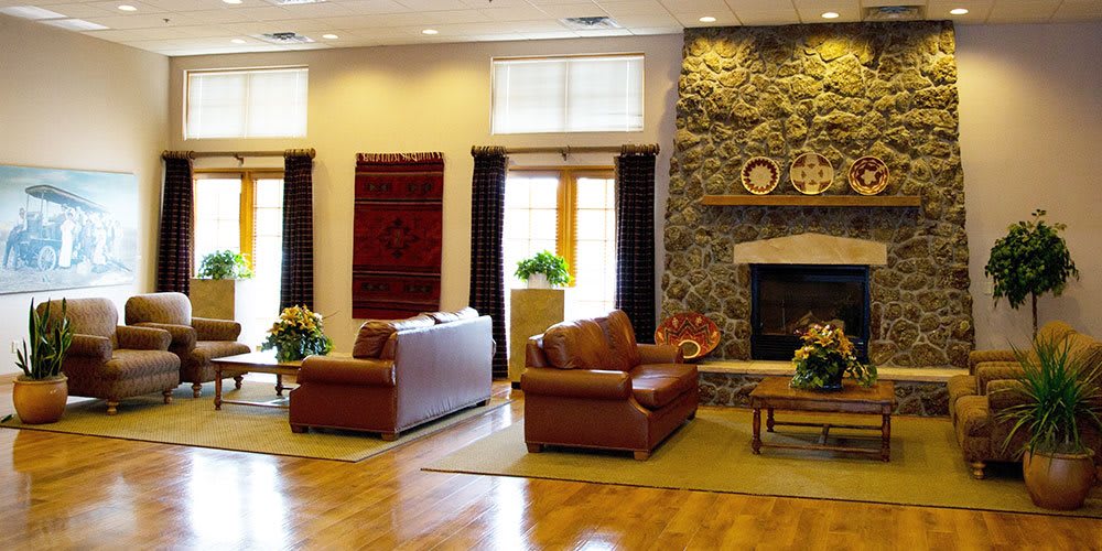 A cozy living room with brown leather couches, a stone fireplace, and large windows letting in natural light.