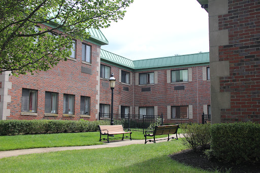 A view of a brick building on a college campus, featuring green roofs and benches in the surrounding lawn.