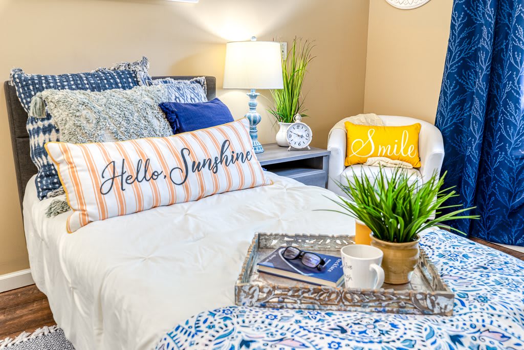A cozy bedroom with inviting decor, featuring decorative pillows, a potted plant, and a warm lamp glow.