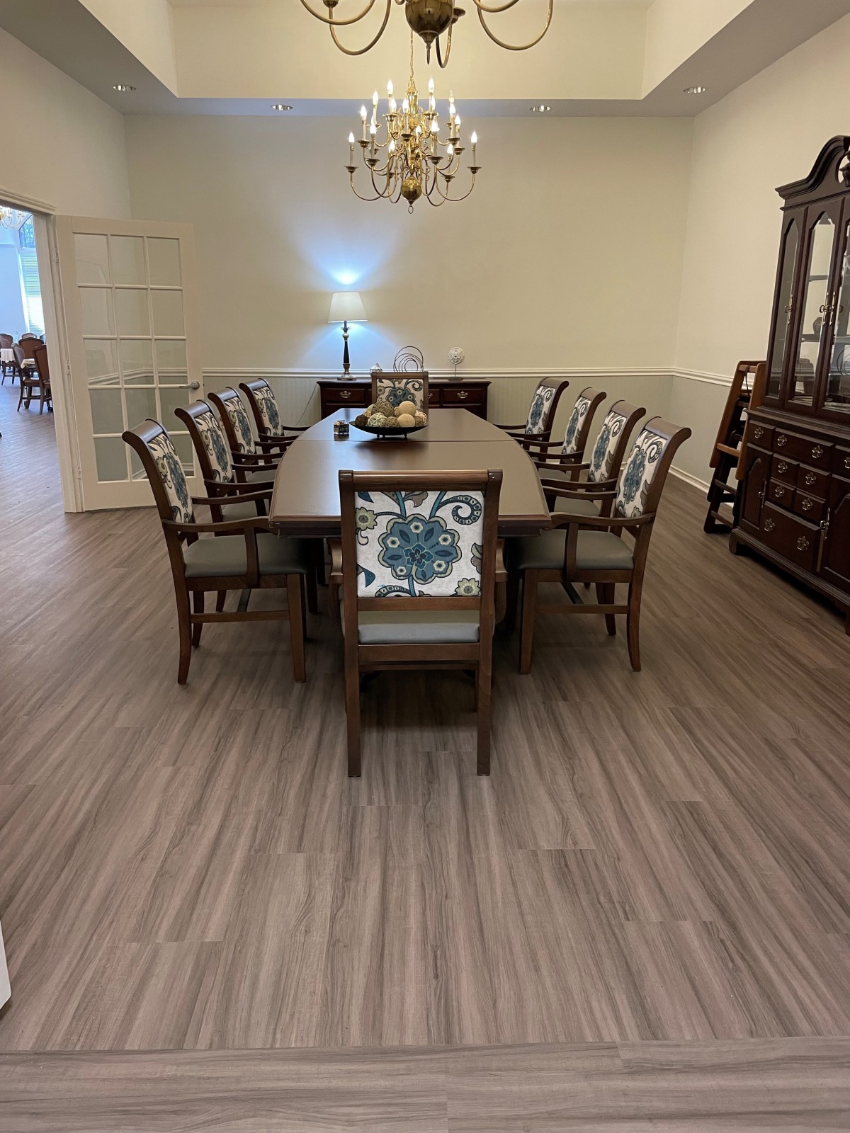 An elegant dining room with a long wooden table surrounded by chairs and illuminated by a chandelier.