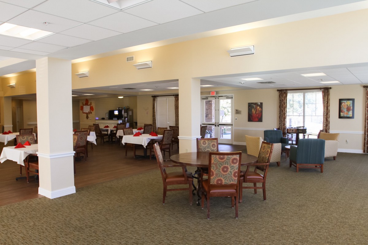 A spacious dining area with tables and chairs arranged neatly, illuminated by ceiling lights and natural light from the windows.