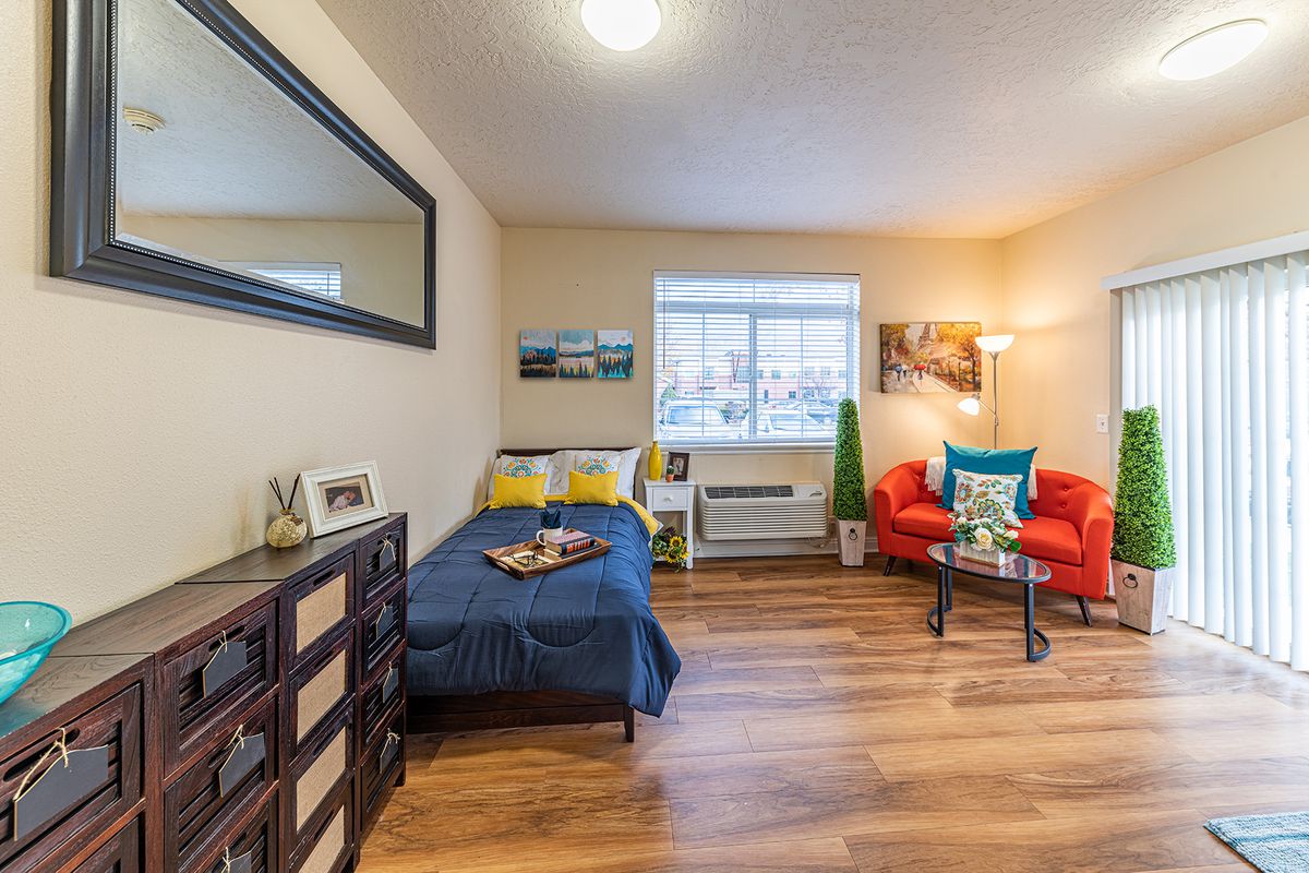 A cozy modern bedroom with a single bed, wood flooring, and a small living area.