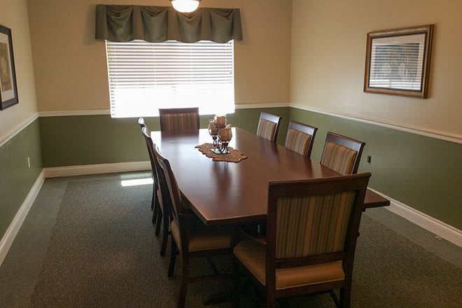 A neatly arranged dining room with a long wooden table and several chairs around it, situated by a window.