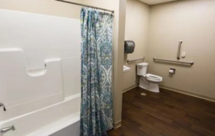 An accessible bathroom featuring a toilet, bathtub with shower curtain, and handrails.