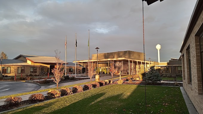 A building at sunset with flags and trees in the foreground under a cloudy sky.