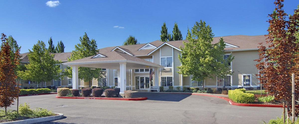 A two-story residential building with a front entrance and surrounding trees.