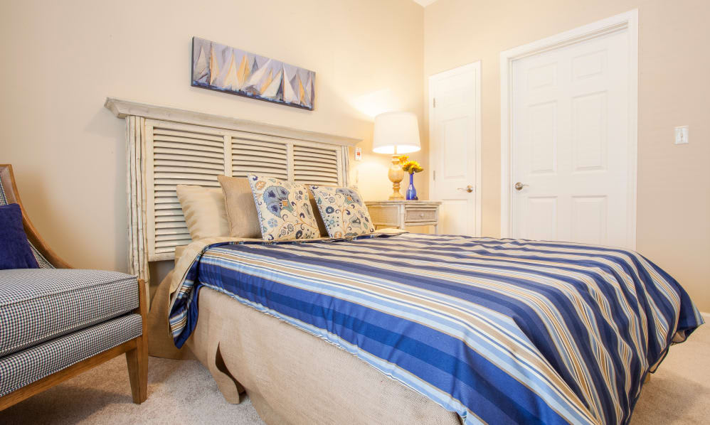 A cozy bedroom with a neatly made bed featuring striped bedding and decorative pillows, illuminated by a bedside lamp.