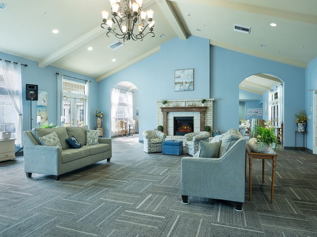 A spacious and elegantly designed living room featuring blue walls, plush sofas, a central fireplace, and a chandelier under a vaulted ceiling.