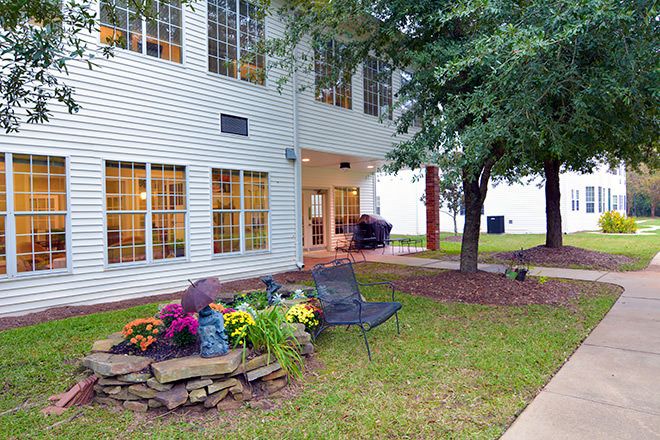 A view of a building exterior with a landscaped garden area featuring chairs and vibrant plants.