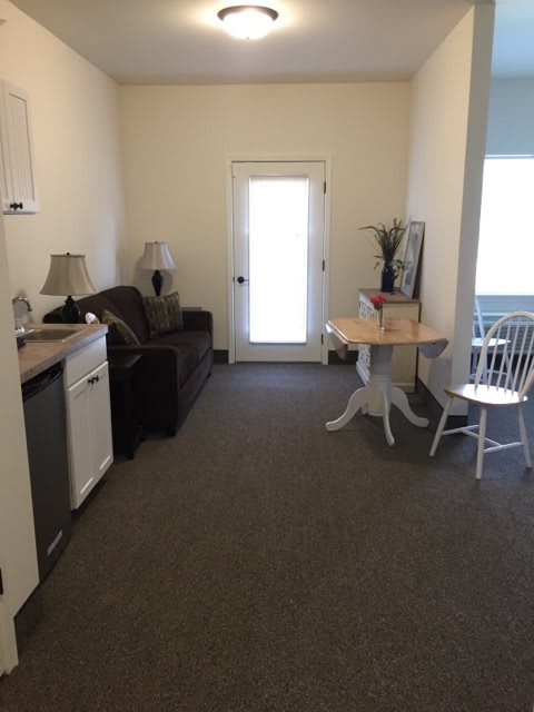 A cozy living room with a sofa, small dining table, and chairs next to a door.