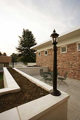 A cozy patio area with outdoor seating, bordered by brick walls and garden beds, featuring a classic black lamp post.
