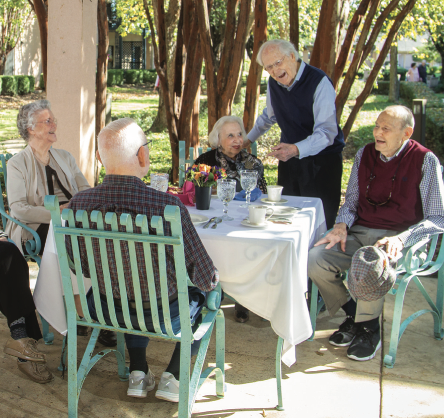 A group of elderly people enjoying a social gathering outdoors around a table.