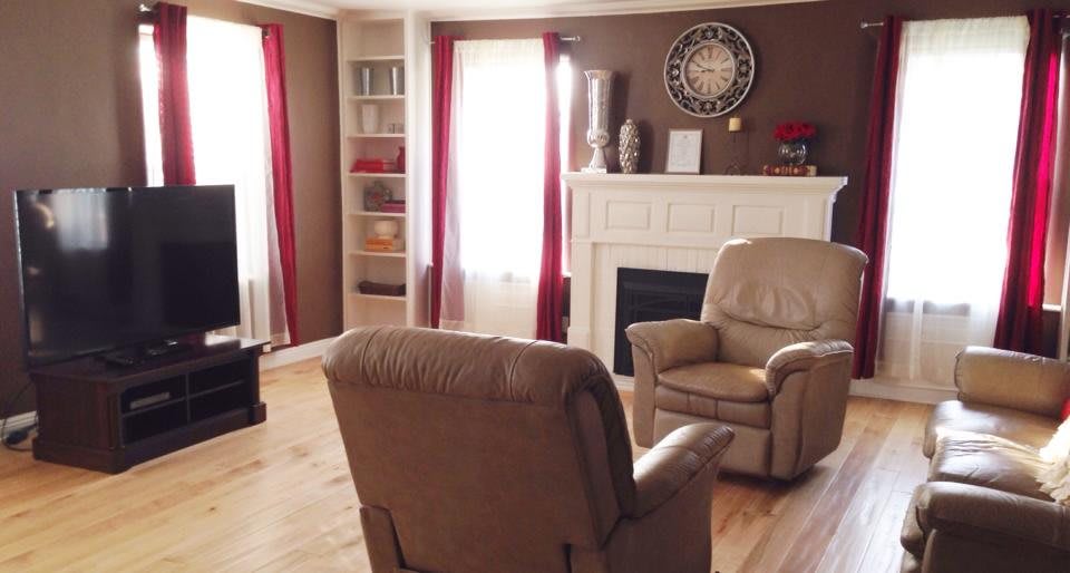 A cozy living room with armchairs, a fireplace, and a large wall clock.