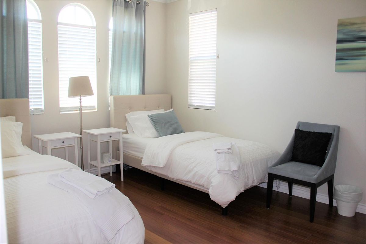A minimalist bedroom with two twin beds, white bedding, and a wooden floor.