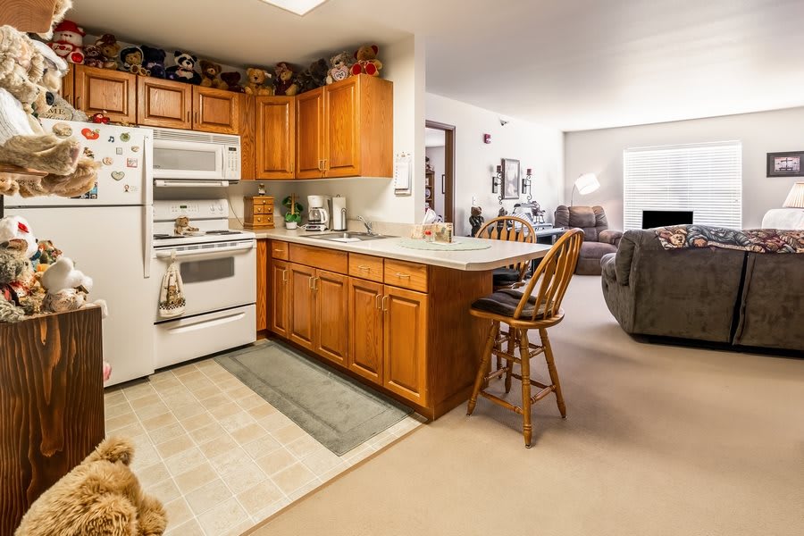 A cozy kitchen with wood cabinets and a view into the living area, featuring a countertop with stools.