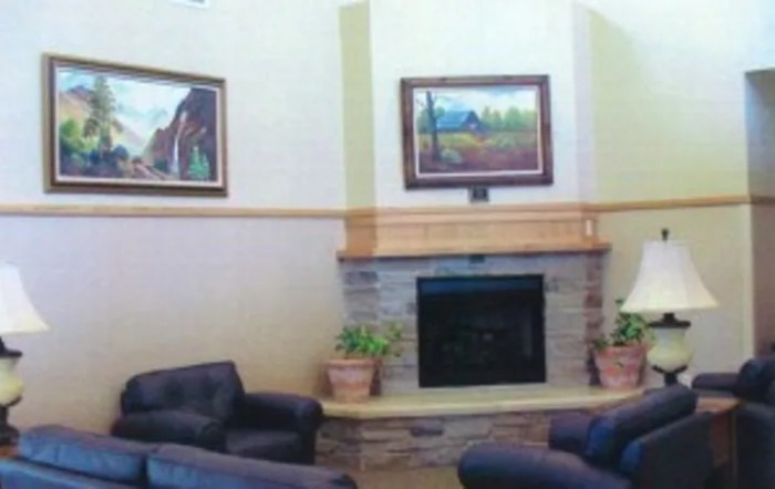 A cozy living room with a fireplace, surrounded by comfortable seating and adorned with paintings and potted plants.