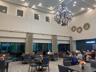 A spacious dining area with a large chandelier, where people are seated at tables.