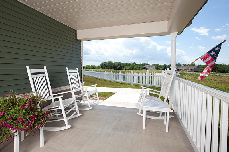 A cozy porch with white rocking chairs overlooking a fenced-in yard.
