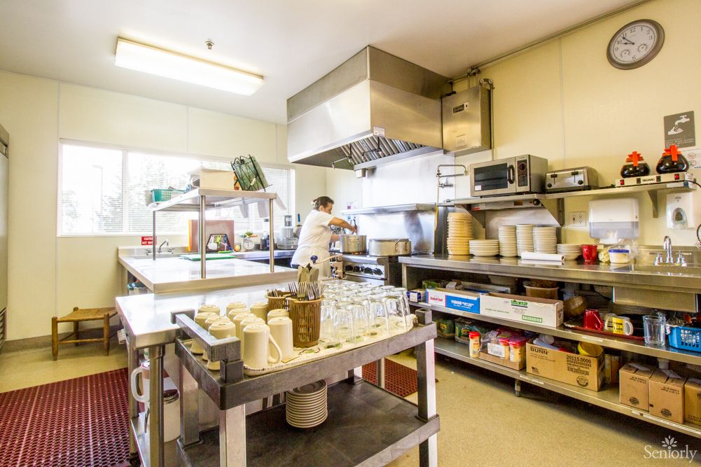 A bustling commercial kitchen with a chef preparing food amidst stainless steel equipment and shelves stocked with various ingredients.