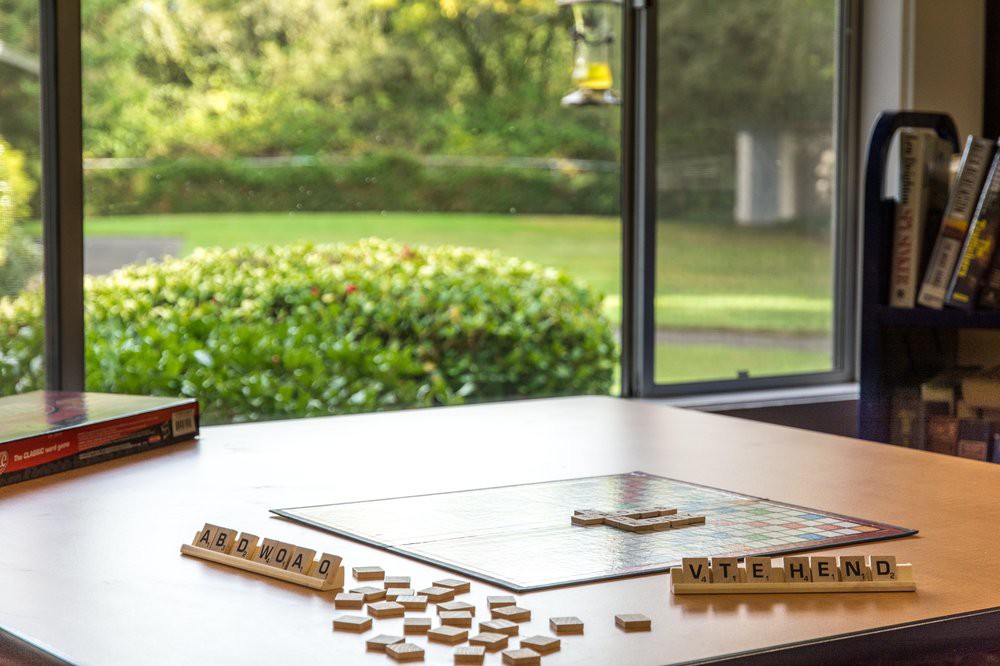 A Scrabble board with tiles scattered on a table by a window overlooking a garden.