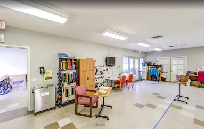 A spacious classroom with chairs, tables, and storage units, featuring a television on the wall.