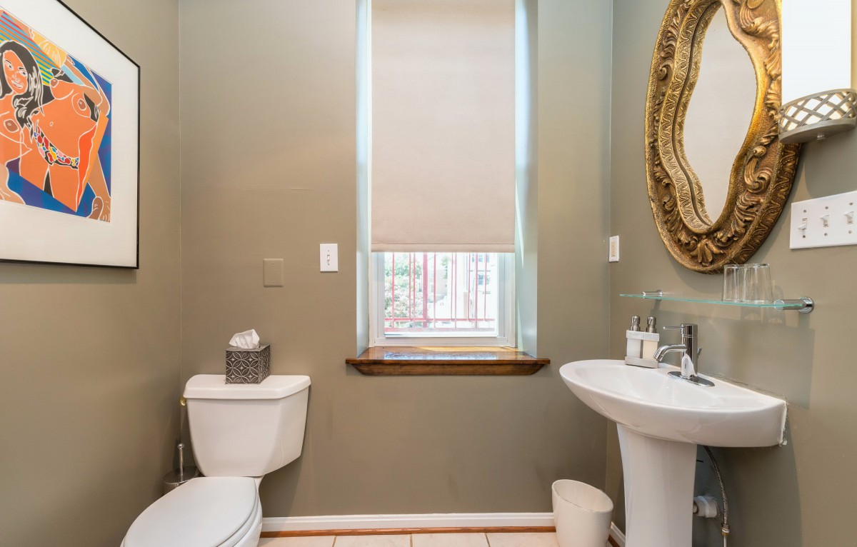 A neatly decorated bathroom with a toilet, sink, and ornate mirror beside a window.
