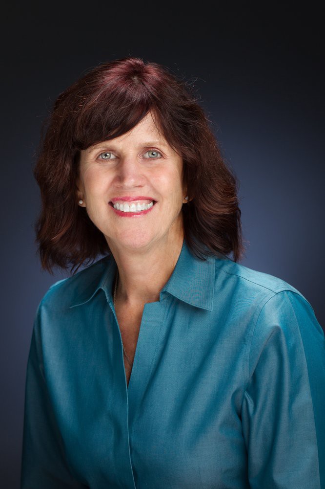 A smiling woman in a teal shirt posing for a portrait.