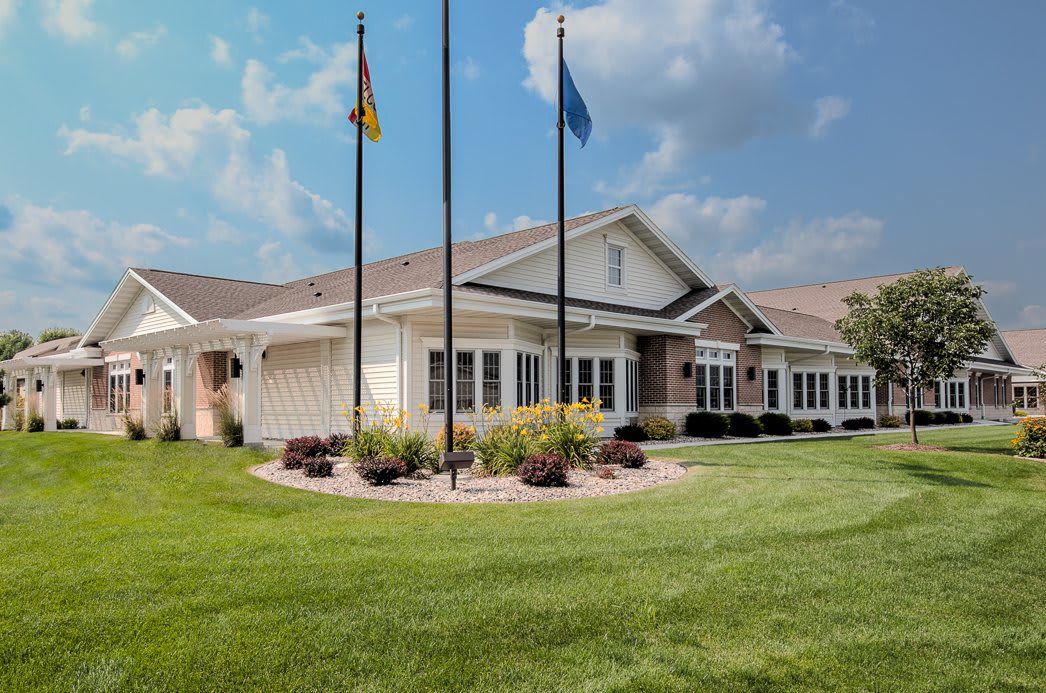 A well-maintained building with flags in front, surrounded by a neatly manicured lawn and landscaping under a partly cloudy sky.