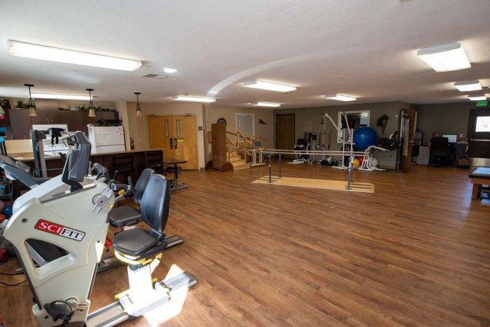 A spacious gym with various exercise equipment and a wooden floor.