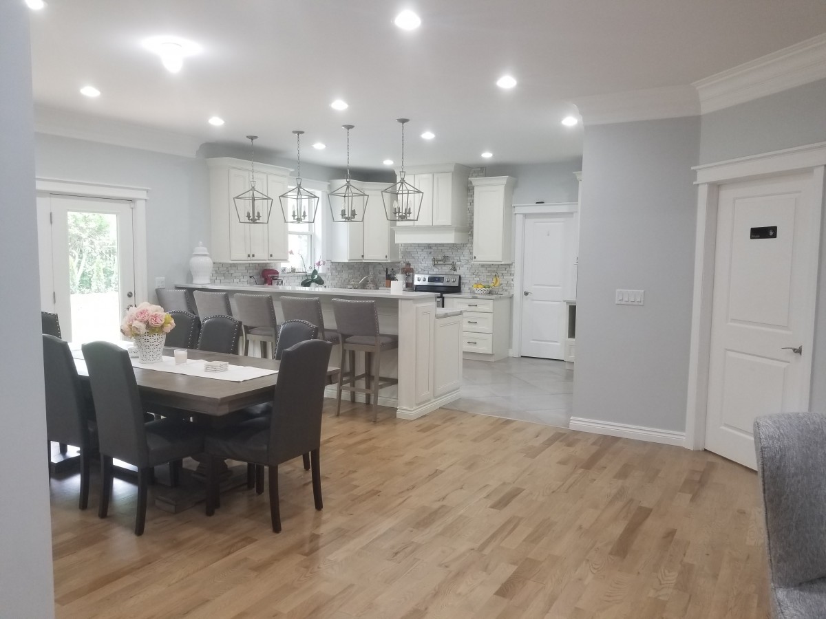 A modern kitchen and dining area with an open layout, featuring hardwood floors, pendant lighting, and a breakfast bar with stools.