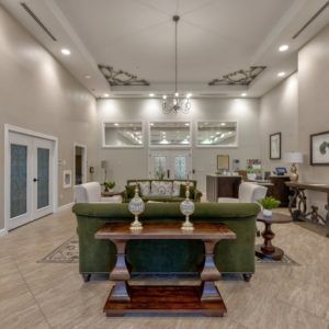 Spacious living room with elegant interior design, featuring a green sofa and high ceilings adorned with chandeliers.