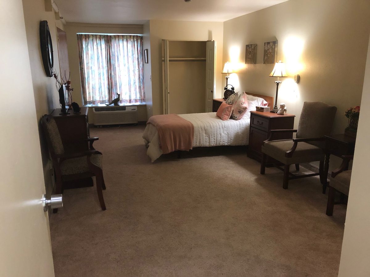 A cozy bedroom with a neatly made bed, chairs, bedside lamps, and a large window.