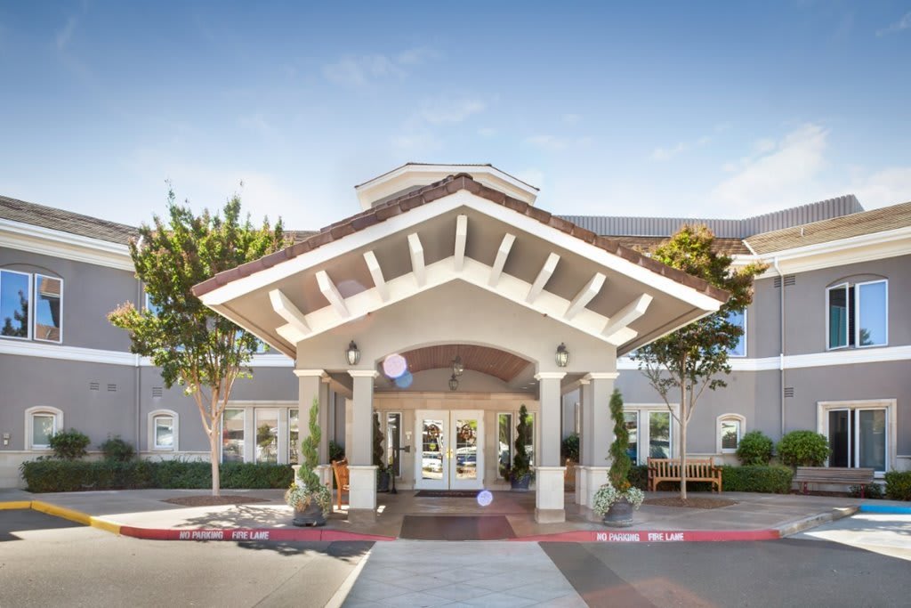 The front entrance of a modern building with an overhang and landscaped surroundings.
