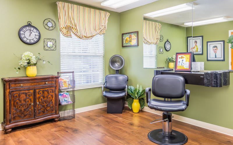 A cozy hair salon interior with green walls, featuring hair styling chairs and a large mirror.
