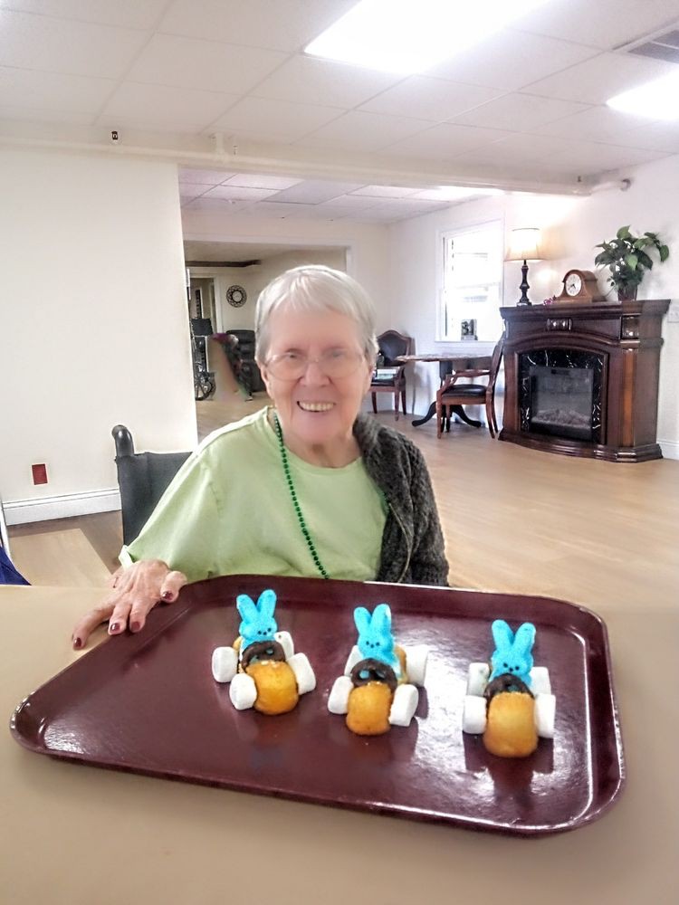 An elderly woman smiling while showcasing a tray of bunny-themed desserts.