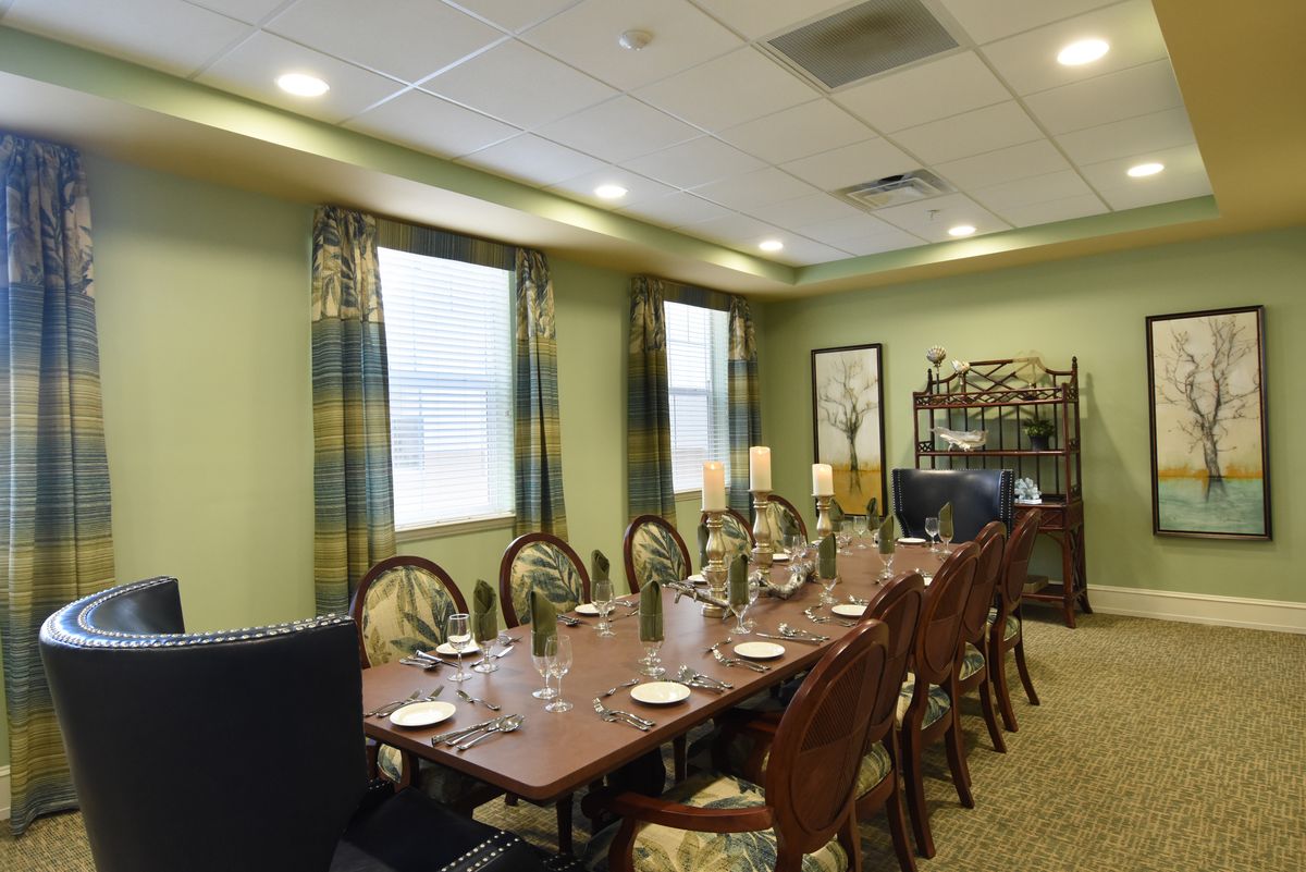 A well-decorated dining room with a long table set for a meal, surrounded by elegant chairs and natural lighting from large windows.