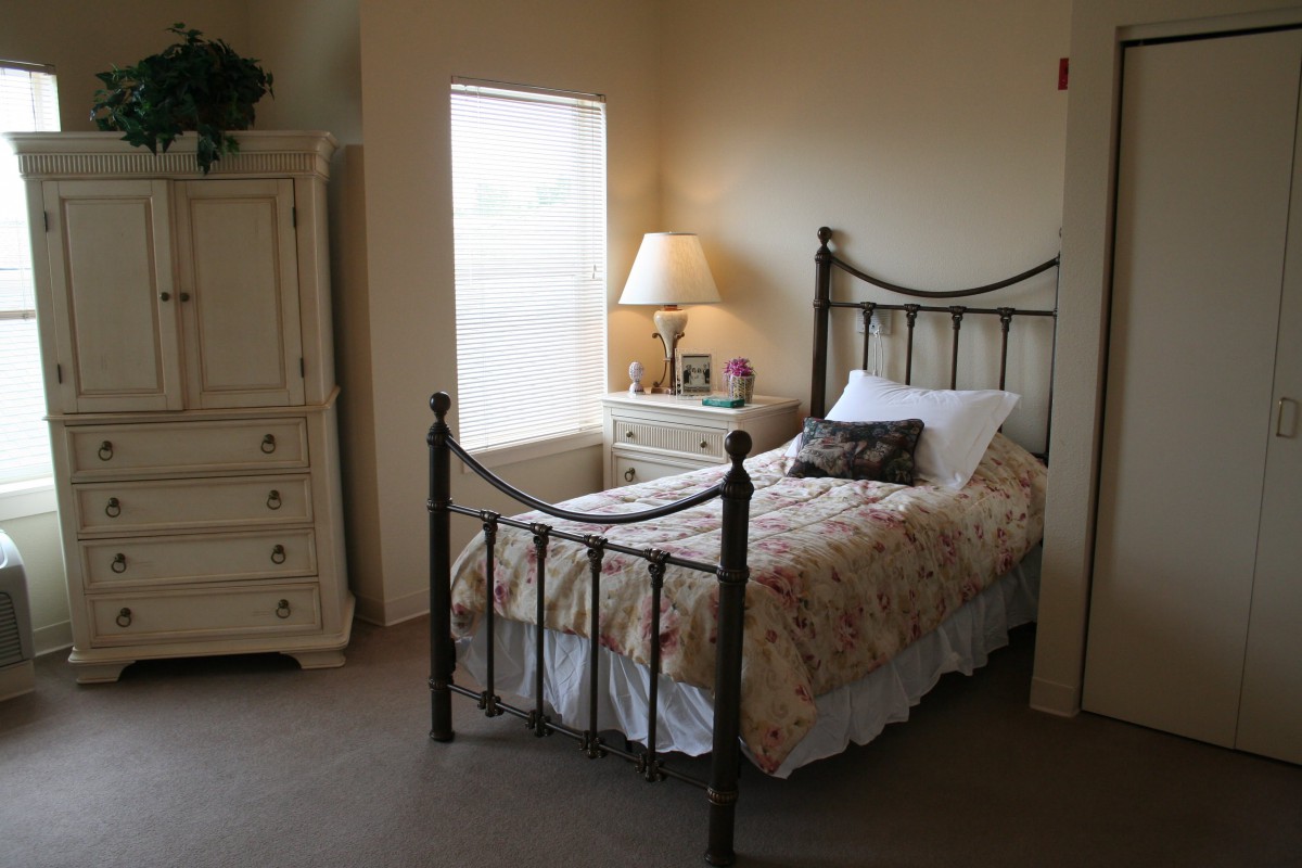 A cozy bedroom with a single metal-framed bed, bedside lamp, and dresser.