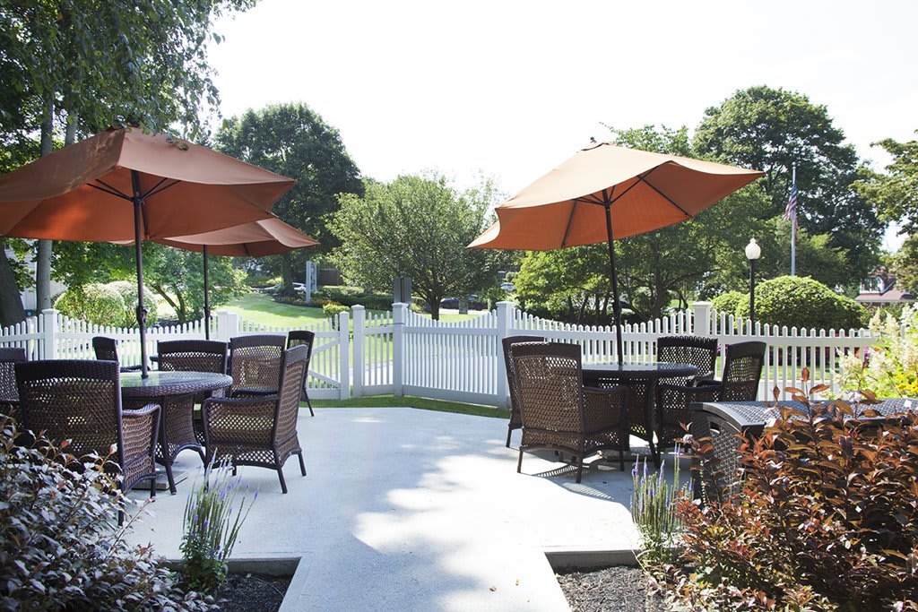 A peaceful outdoor patio area with tables, chairs, and umbrellas set against a garden backdrop.