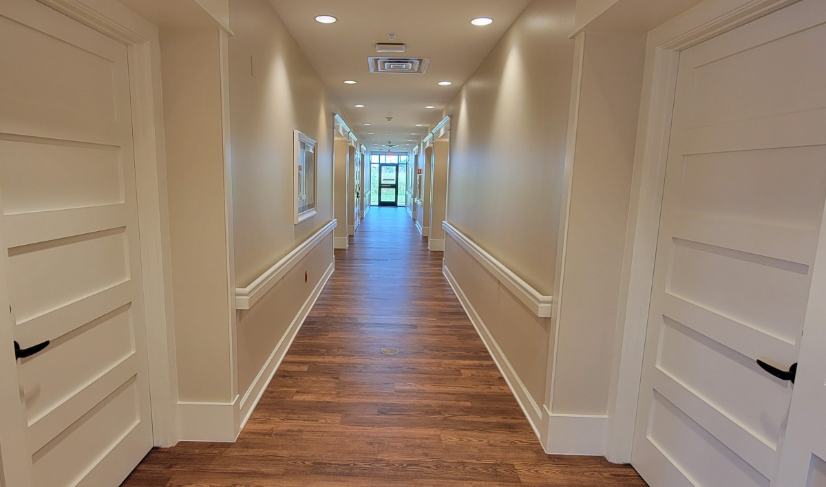 A long, bright hallway with wooden flooring and overhead lighting.