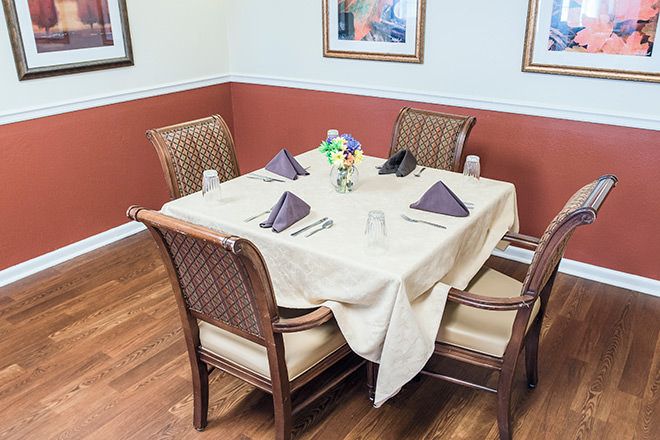A neatly set dining table with four chairs, adorned with napkins and a flower centerpiece in a cozy restaurant setting.